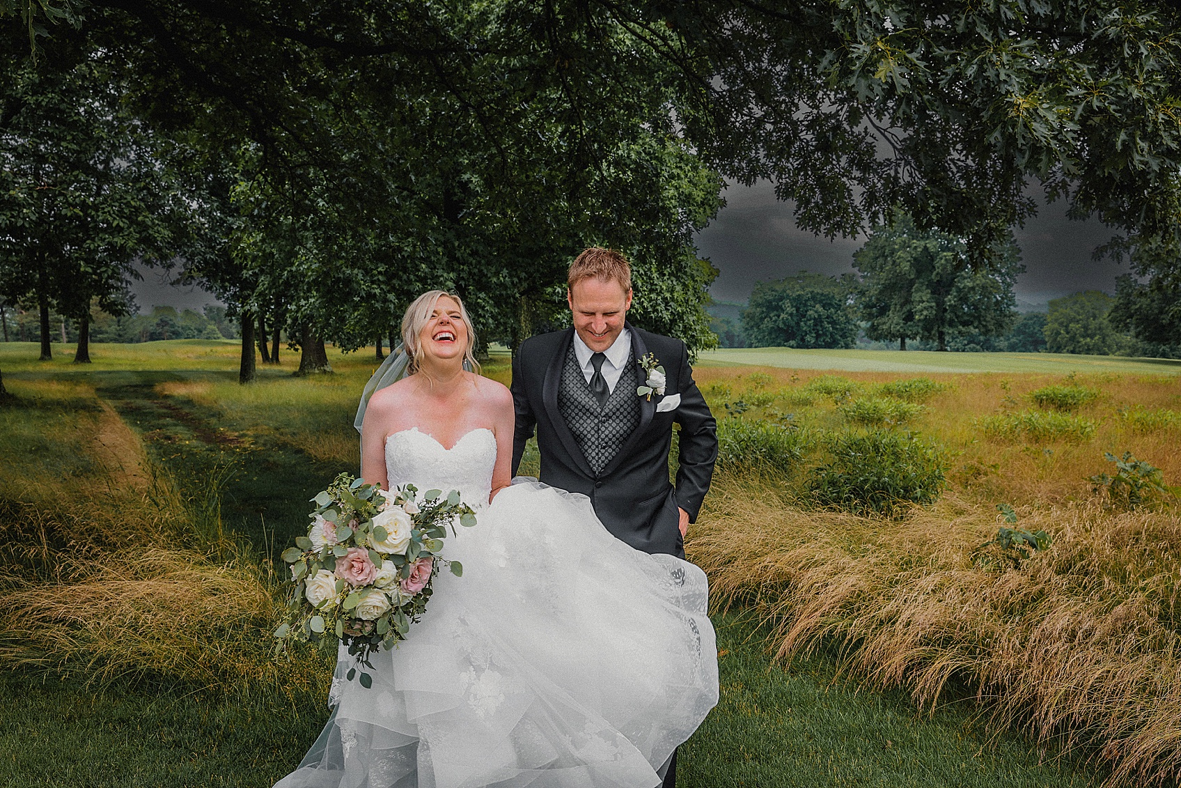 bride and groom walking thru a field during a thunderstorm on their wedding day